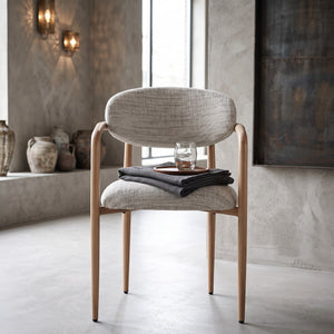 Rustgevende interieursetting met een strakke gietvloer en sfeervolle wandverlichting, waarin de Okura armstoel met een houten dienblad en glas water direct een serene Japandi-sfeer uitstraalt.