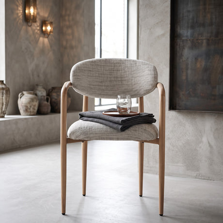 Rustgevende interieursetting met een strakke gietvloer en sfeervolle wandverlichting, waarin de Okura armstoel met een houten dienblad en glas water direct een serene Japandi-sfeer uitstraalt.