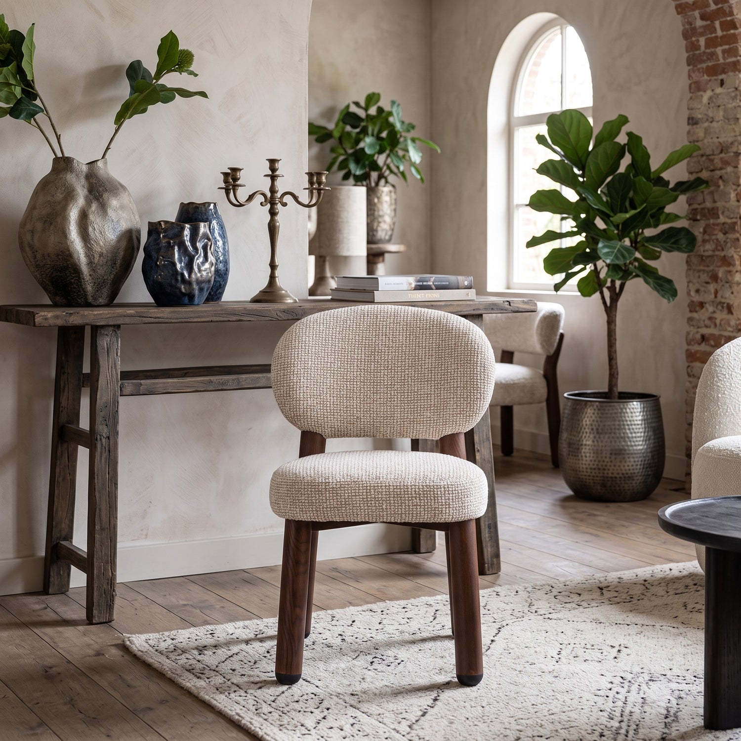 Vooraanzicht van de sculpturale Oatly eetkamerstoel op een geweven vloerkleed, omringd door een houten sidetable met aardewerk vazen, kandelaar en een grote plant in een bronzen pot.