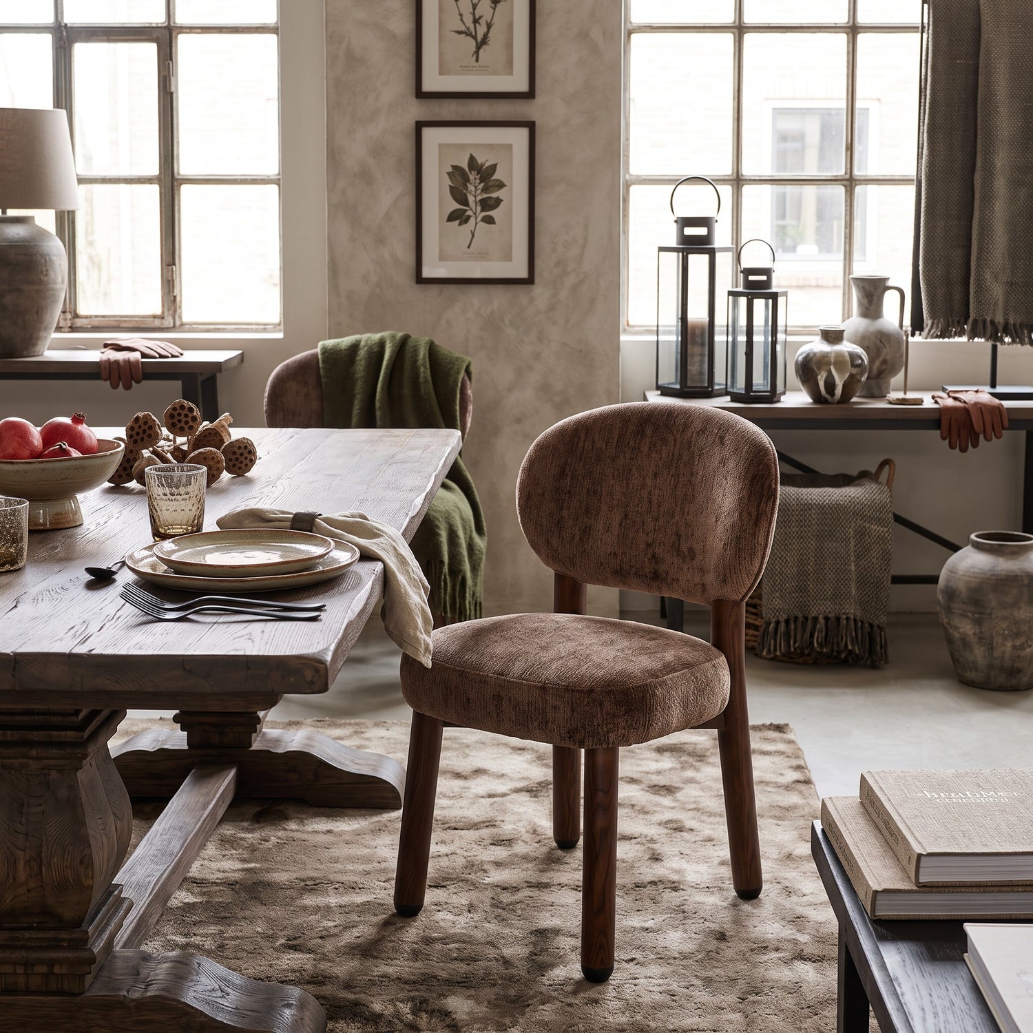 De sculpturale Umber eetkamerstoel met spring pocket zitting, sfeervol geplaatst aan een doorleefde houten eettafel met aardewerk servies, lantaarns en botanische wanddecoratie.