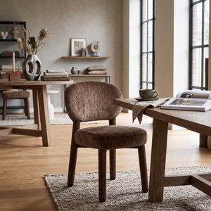 Een harmonieuze lifestyle-setting waarin de Umber designstoel tot zijn recht komt aan een houten tafel met koffiekop en open boek, geplaatst op een grof geweven vloerkleed in een lichte ruimte.