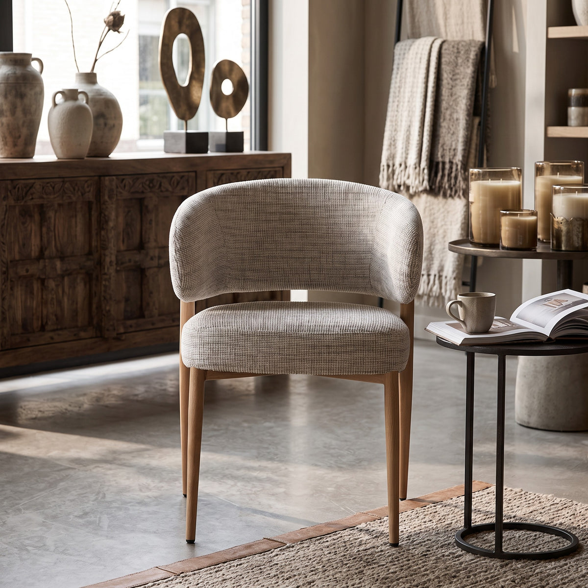 Een sfeervol interieurbeeld waarin de armstoel Okura als rustgevend designelement staat. Het warme houten dressoir, de bijzettertjes met kaarsen en het vloerkleed creëren een harmonieuze en uitnodigende hotel-chique ambiance.