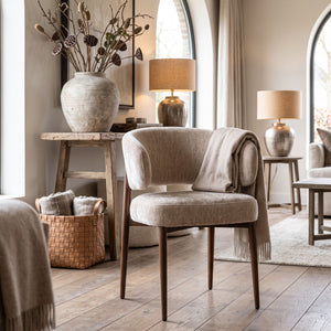 Een sfeervol interieurbeeld waarin de armstoel Tan als rustgevend designelement staat. De hotel-chique ambiance wordt versterkt door het houten dressoir, de bijzettertjes met kaarsen en de zachte plaids, wat zorgt voor een harmonieuze en uitnodigende sfeer.