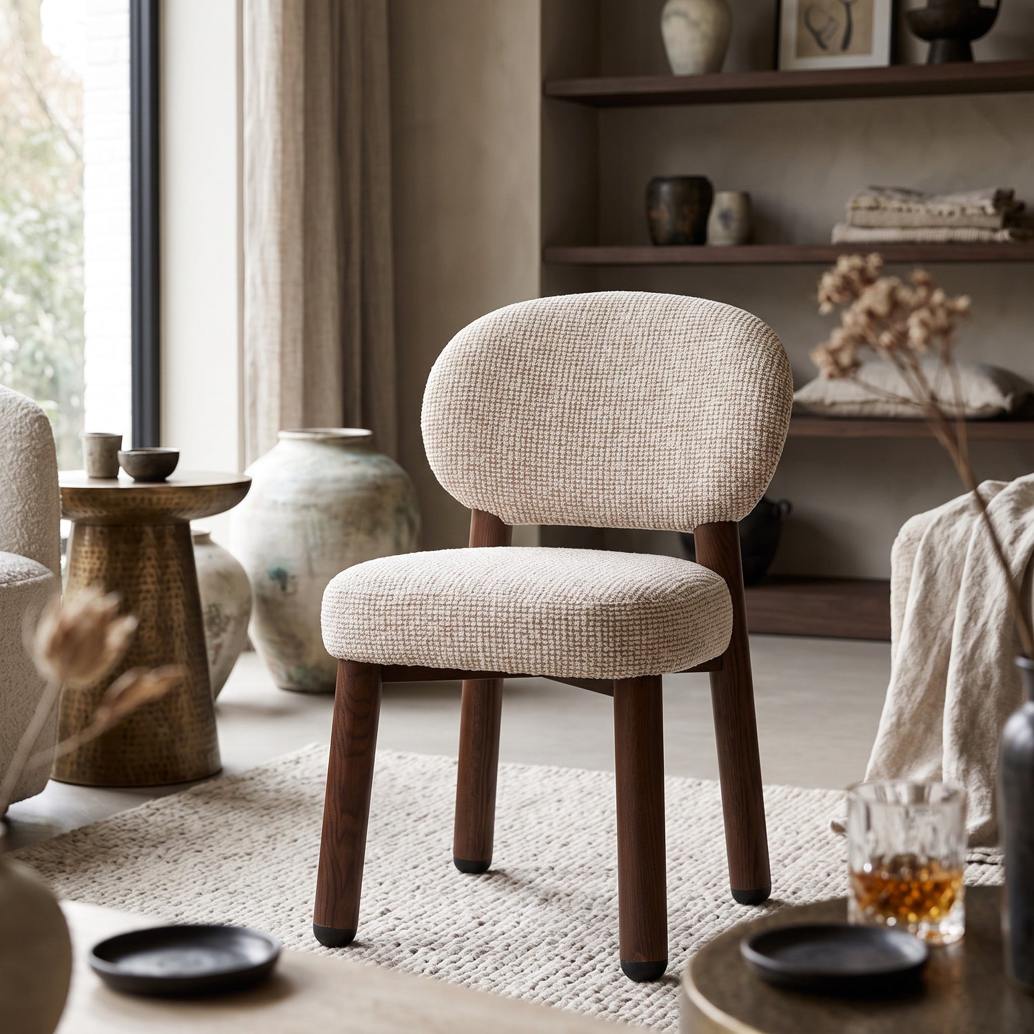 Een warme lifestyle-setting waarin de Oatly stoel met pocketvering zitting tot zijn recht komt naast een messing bijzettafel, open vakkenkast en zachte linnen plaids.