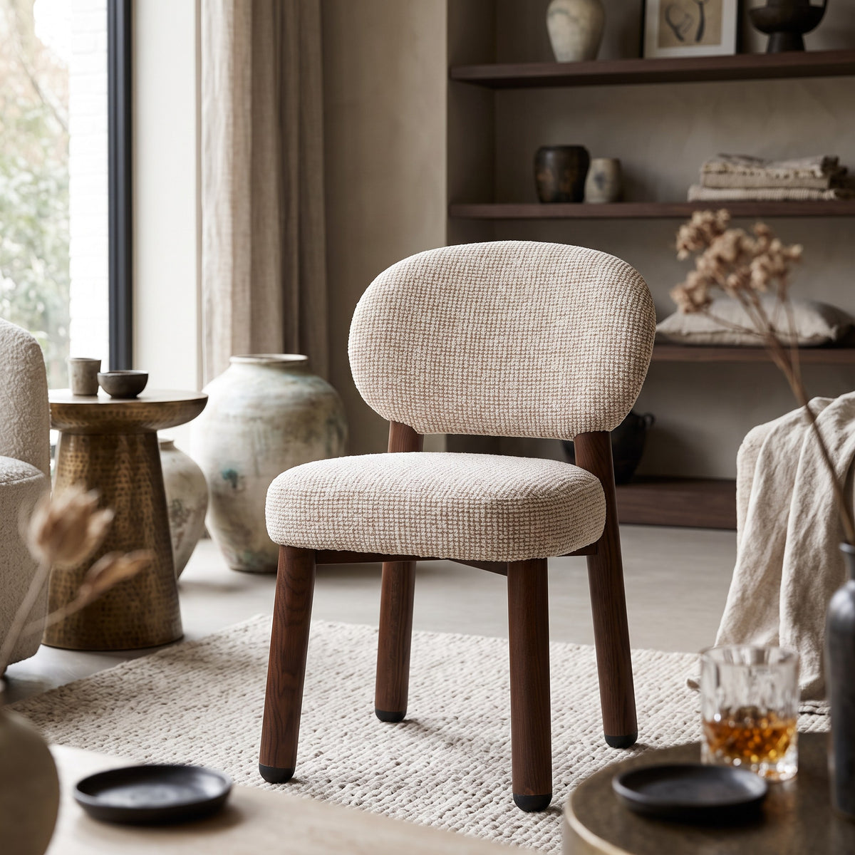 Een warme lifestyle-setting waarin de Oatly stoel met pocketvering zitting tot zijn recht komt naast een messing bijzettafel, open vakkenkast en zachte linnen plaids.