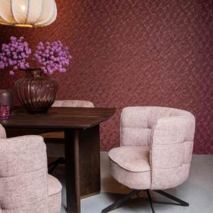 Een sfeervolle hotel-chique eethoeksetting met de zachtroze draaistoel aan een donkere eettafel, gedecoreerd met een glazen vaas met paarse bloemen en een warme bordeauxrode wandafwerking.